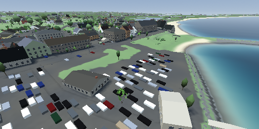 Old Harbor from above: hotels along a street, a car park full of parked cars, green lawn and the beach curving away east